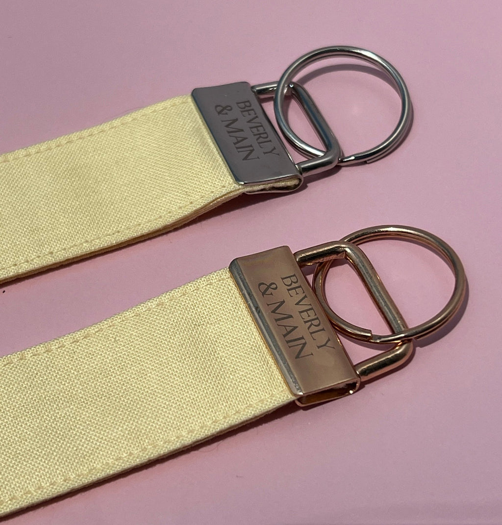 Yellow wristlet keychains with silver and gold hardware with 'Beverly & Main' branding on a pink background.