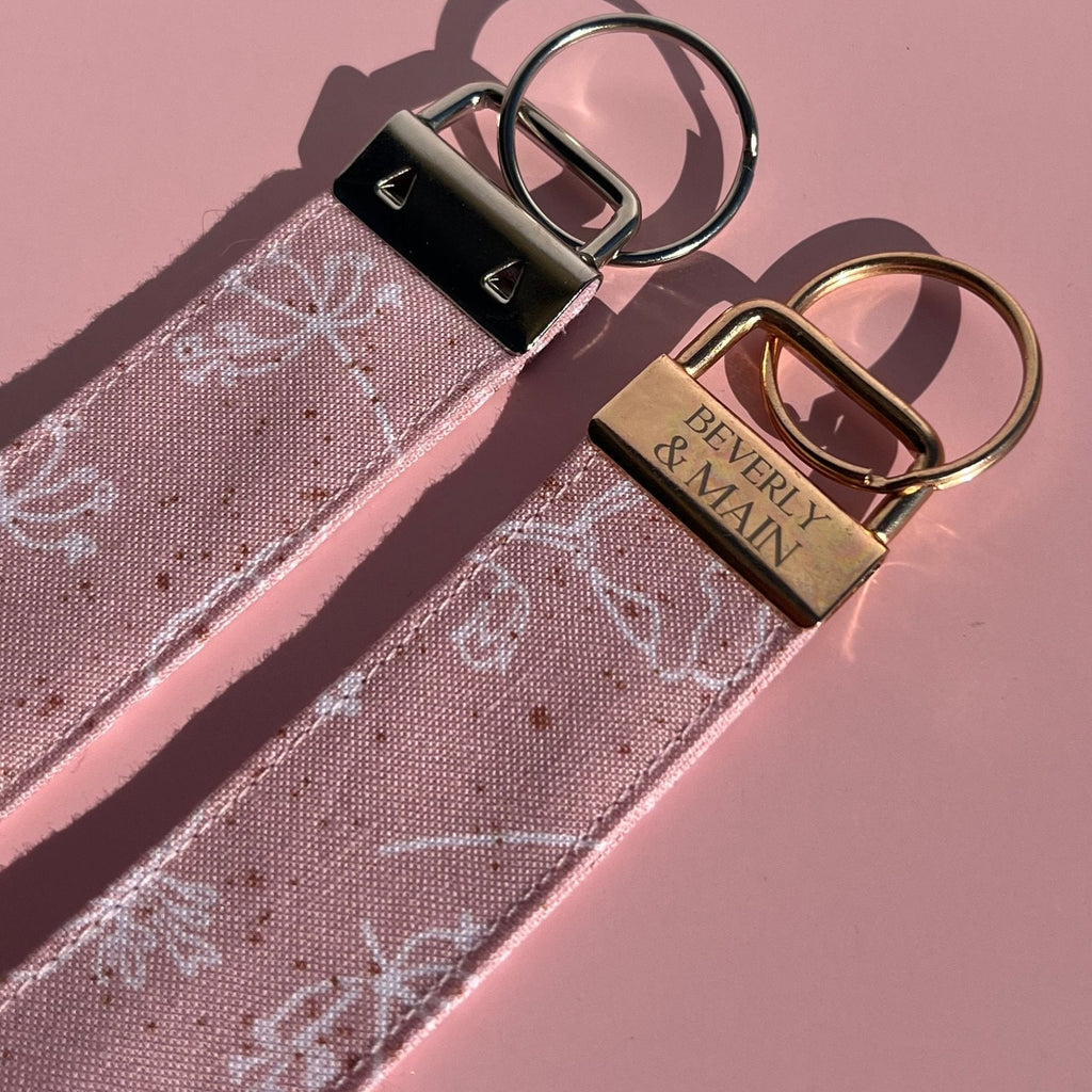 Pink fabric wristlet keychains with floral line art and gold or silver hardware by Beverly & Main